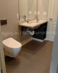 tile barrier free shower with built in shower seat for wheelchair accessibility, bathroom includes a wall mounted toilet and roll under sink